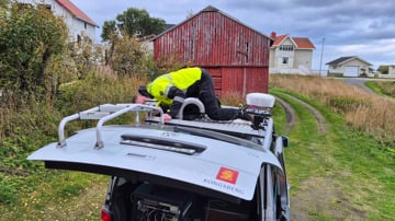 Man on top of car, mounting test equipment.