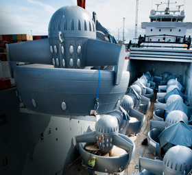 2 rows of thrusters on the deck of a transport ship. One more thruster is being loaded onboard.